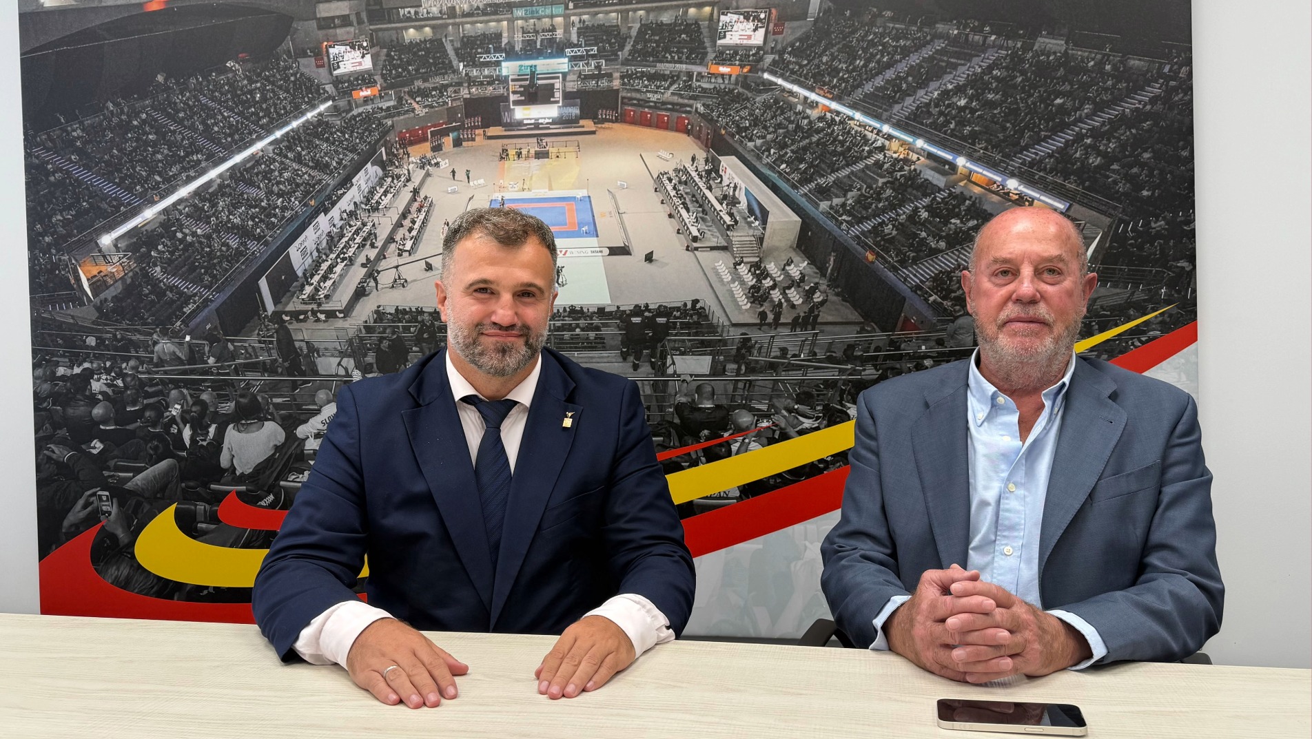 Ukrainian Karate Federation President Ivan Dutchak and WKF President Antonio Espinós seated at a table at WKF headquarters in Madrid, in front of a karate arena photo